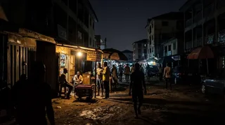 Nigerian street during a power outage at night showing a business relying on a generator while surrounding buildings remain in darkness