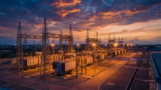 Aerial view of a high-voltage electricity transmission substation in Nigeria at dusk, showing power transformers and steel lattice towers