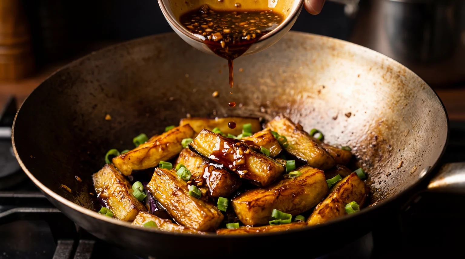 Garlic sauce being poured over seared Chinese eggplant and green onions in a wok