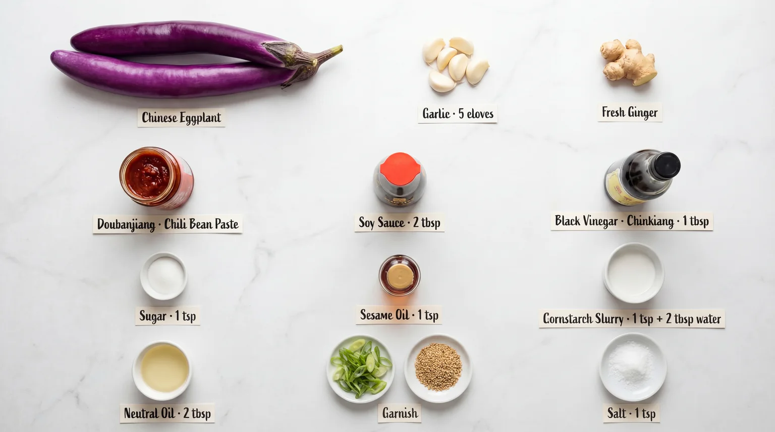 Labelled ingredient flat lay for Chinese Eggplant with Garlic Sauce — eggplant, garlic, ginger, doubanjiang, soy sauce, black vinegar, sesame oil, cornstarch, and garnish on white marble