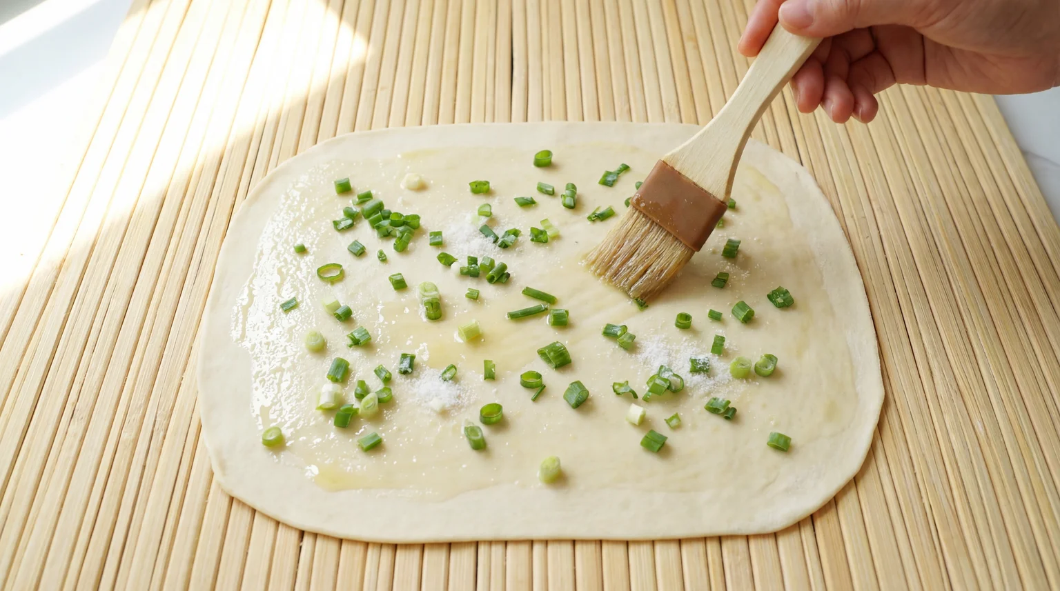 Brushing oil paste on rolled scallion pancake dough with green onions and salt, essential step for creating flaky layers in cong you bing