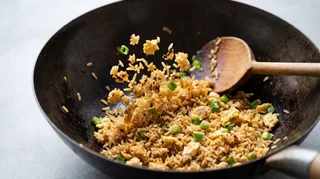 Wok hei technique — egg fried rice at the active tossing stage in a seasoned carbon steel wok, grains golden-brown and separated