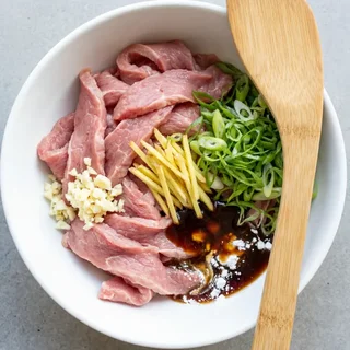 Chinese stir-fry mise en place — raw velveted flank steak, minced garlic, ginger, spring onions, and pre-mixed brown sauce ready before cooking