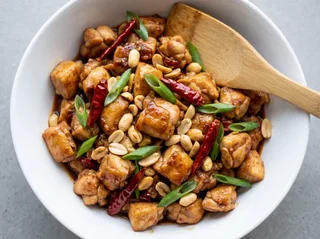 Kung Pao chicken — diced seared chicken thigh with roasted peanuts, dried chillies, and glossy doubanjiang sauce in a white ceramic bowl