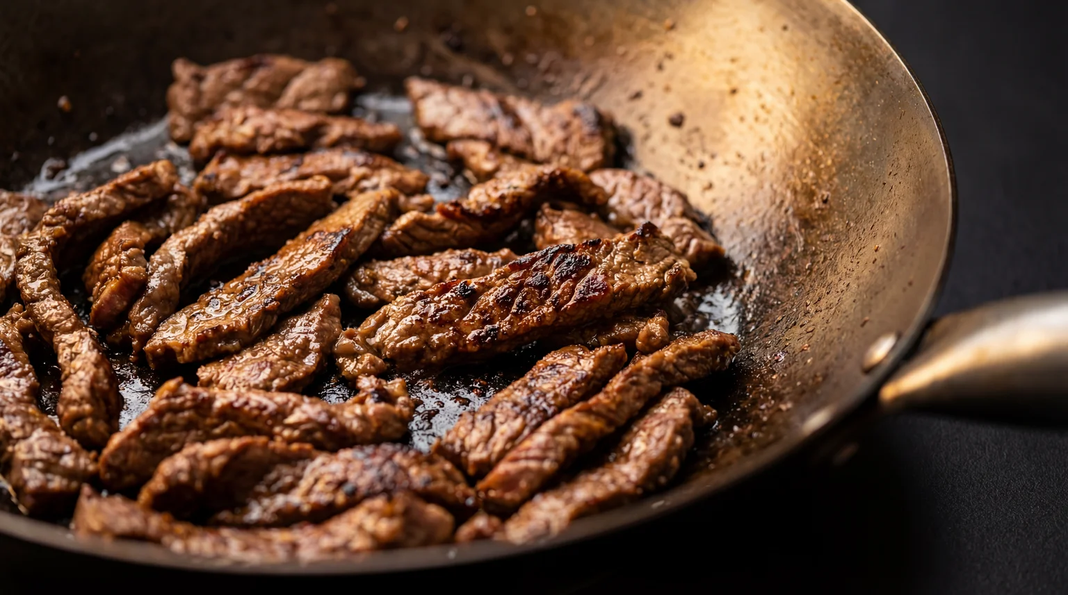 Thinly sliced flank steak searing in a carbon steel wok, caramelized crust and char marks visible on the beef strips, batch-cooking method for pepper steak stir fr