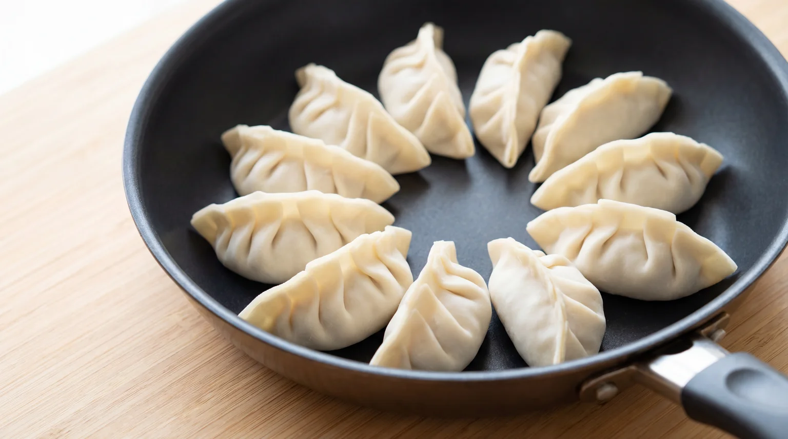 Uncooked gyoza arranged in non-stick skillet, pleated side up in circular pattern ready for steam-frying