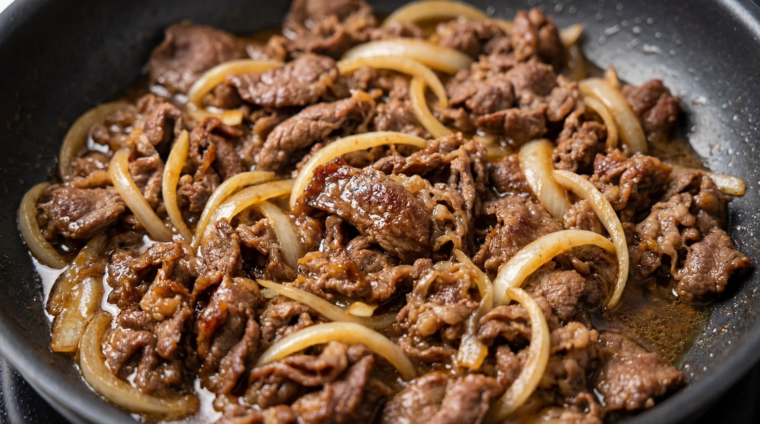 Searing Korean Beef Bulgogi with caramelized onions in cast iron skillet, showing Maillard reaction and glossy sauce reduction