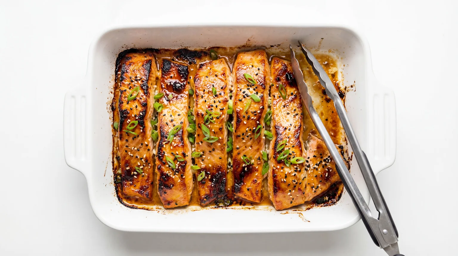Miso glazed salmon fillets in a white baking dish topped with sesame seeds and green onions, showing caramelized edges from miso table sauce marinade