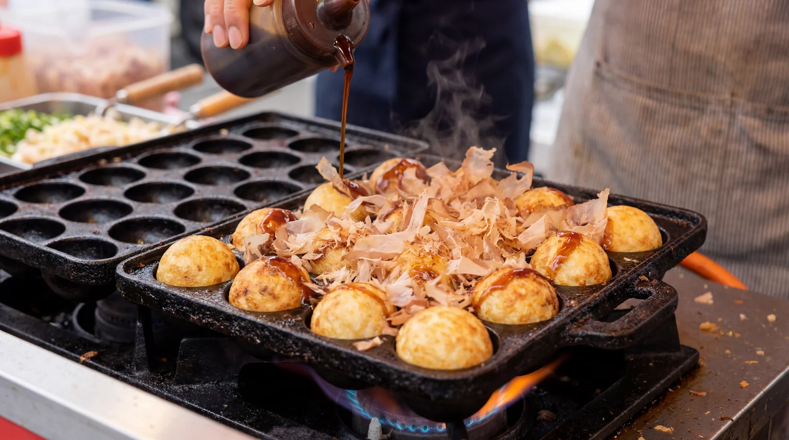 Fresh Takoyaki octopus balls cooking in a cast-iron pan topped with dancing bonito flakes