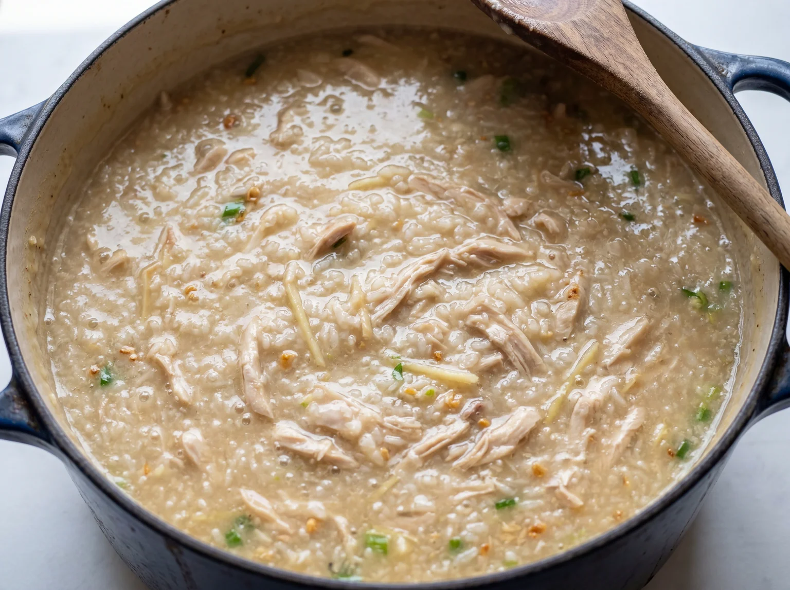 Thick creamy arroz caldo with shredded chicken simmering in a Dutch oven showing the final porridge consistency