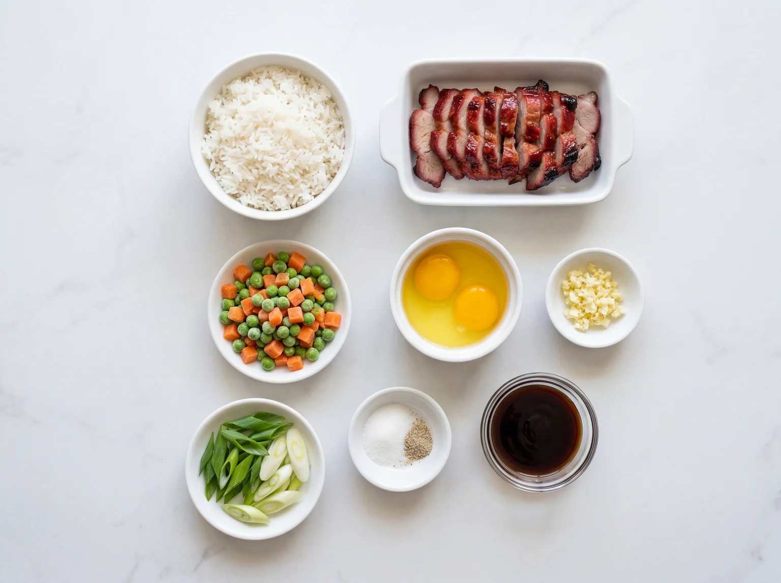 Char siu fried rice ingredients flat-lay including day-old jasmine rice, BBQ pork slices, eggs, garlic, peas, carrots, and sauce bowls