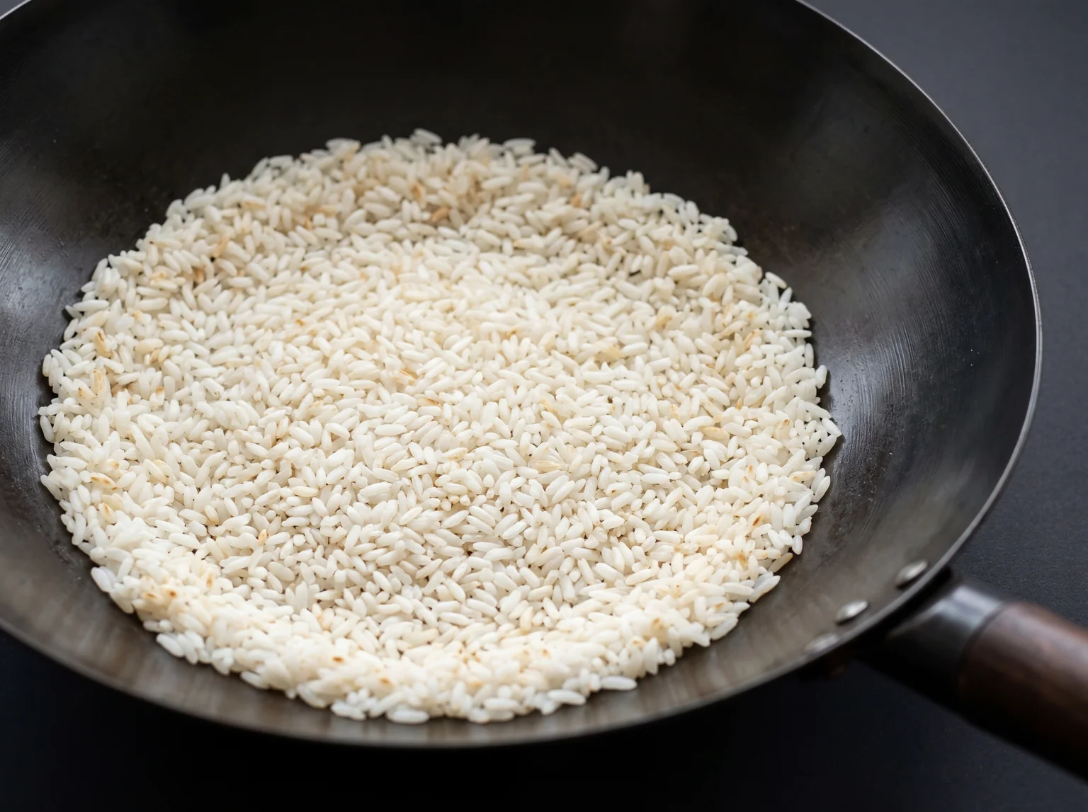 Cooked white day-old jasmine rice grains frying in a clean carbon steel wok, each grain separated with lightly toasted golden edges