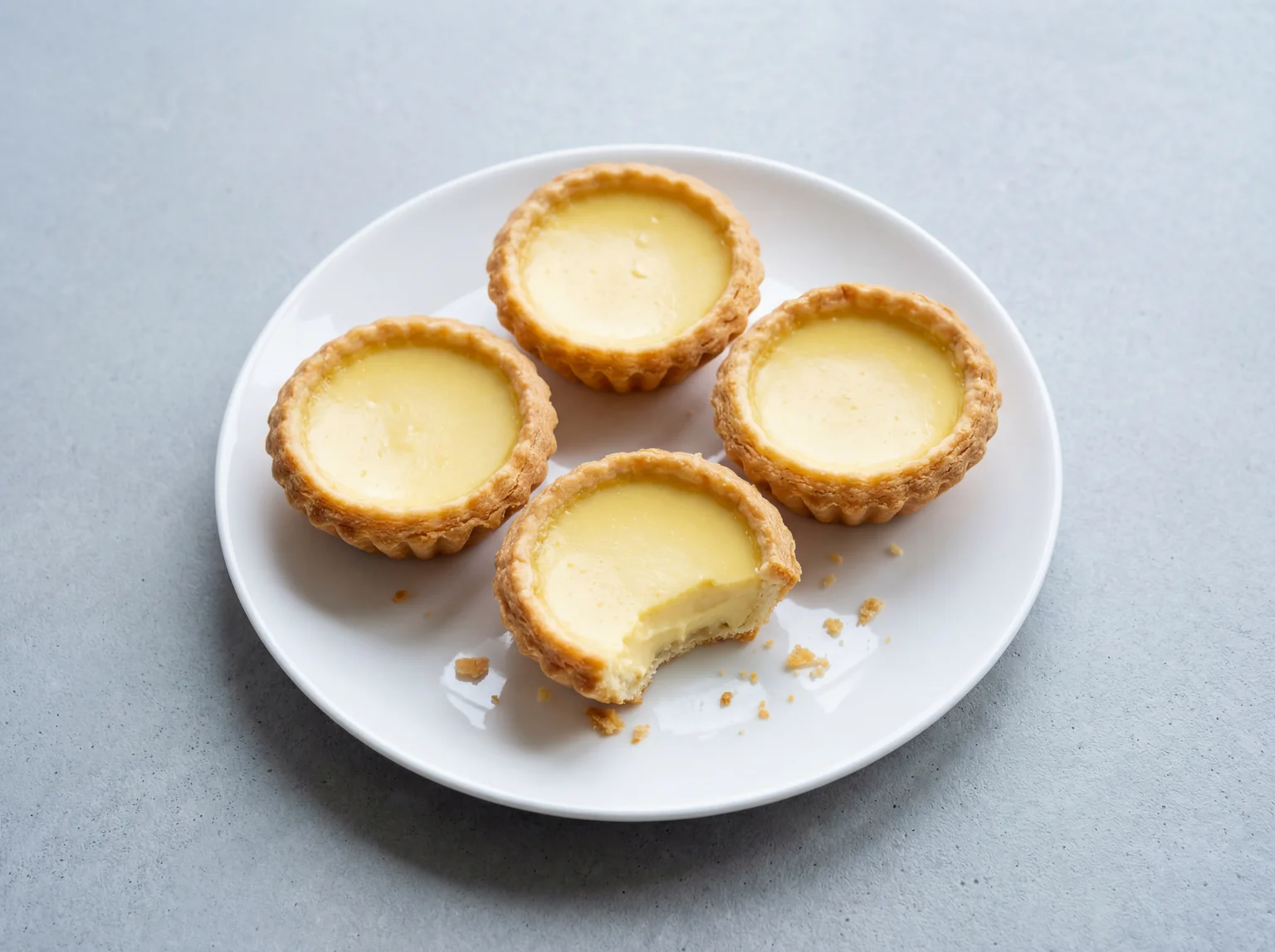 Four freshly baked Chinese egg tarts with golden pastry shells and smooth pale yellow custard on a white ceramic plate