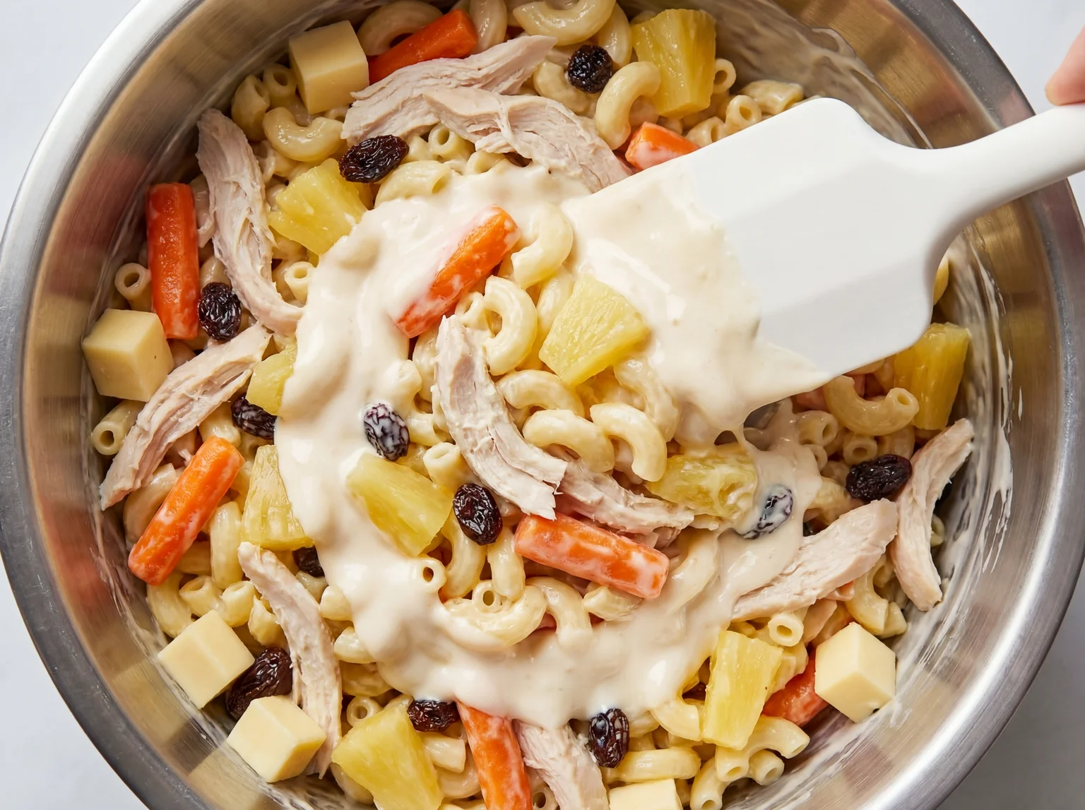 Combining Filipino macaroni salad ingredients in a large mixing bowl
