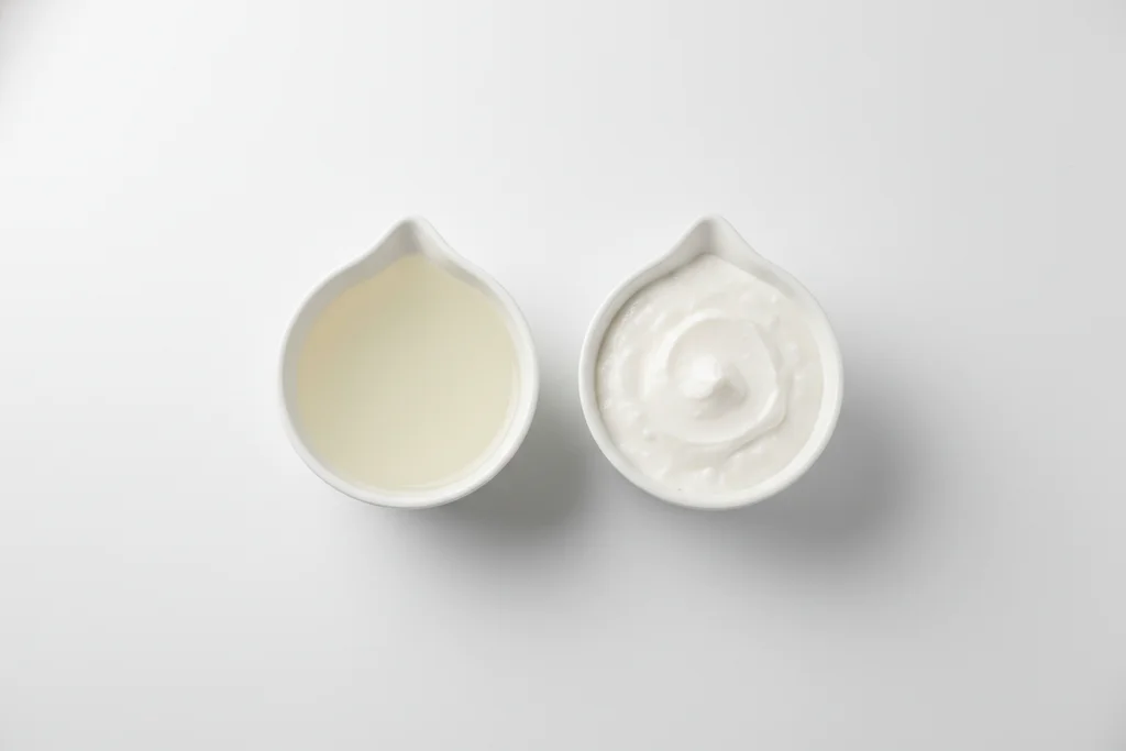 Two small white bowls side by side showing the thinner coconut milk soaking sauce on the left and the thicker coconut cream topping sauce on the right