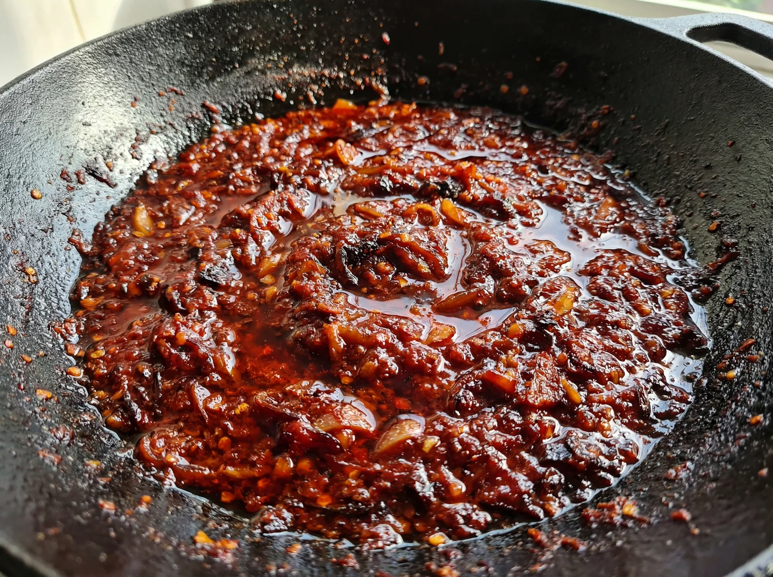 Sambal tumis in a black cast iron wok at the pecah minyak stage — glistening red oil separating from deeply caramelised chili paste